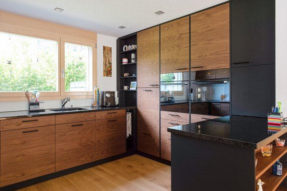 Einbauküche in edlem Nussbaumholz, kombiniert mit schwarz belegten Fronten, V-Zug Geräte auf ergonomischer Höhe eingebaut